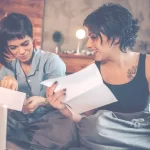 Duas mulheres sorridentes analisando documentos enquanto trabalham em uma estratégia de tráfego pago no conforto de casa.