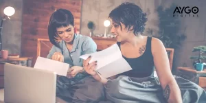 Duas mulheres sorridentes analisando documentos enquanto trabalham em uma estratégia de tráfego pago no conforto de casa.